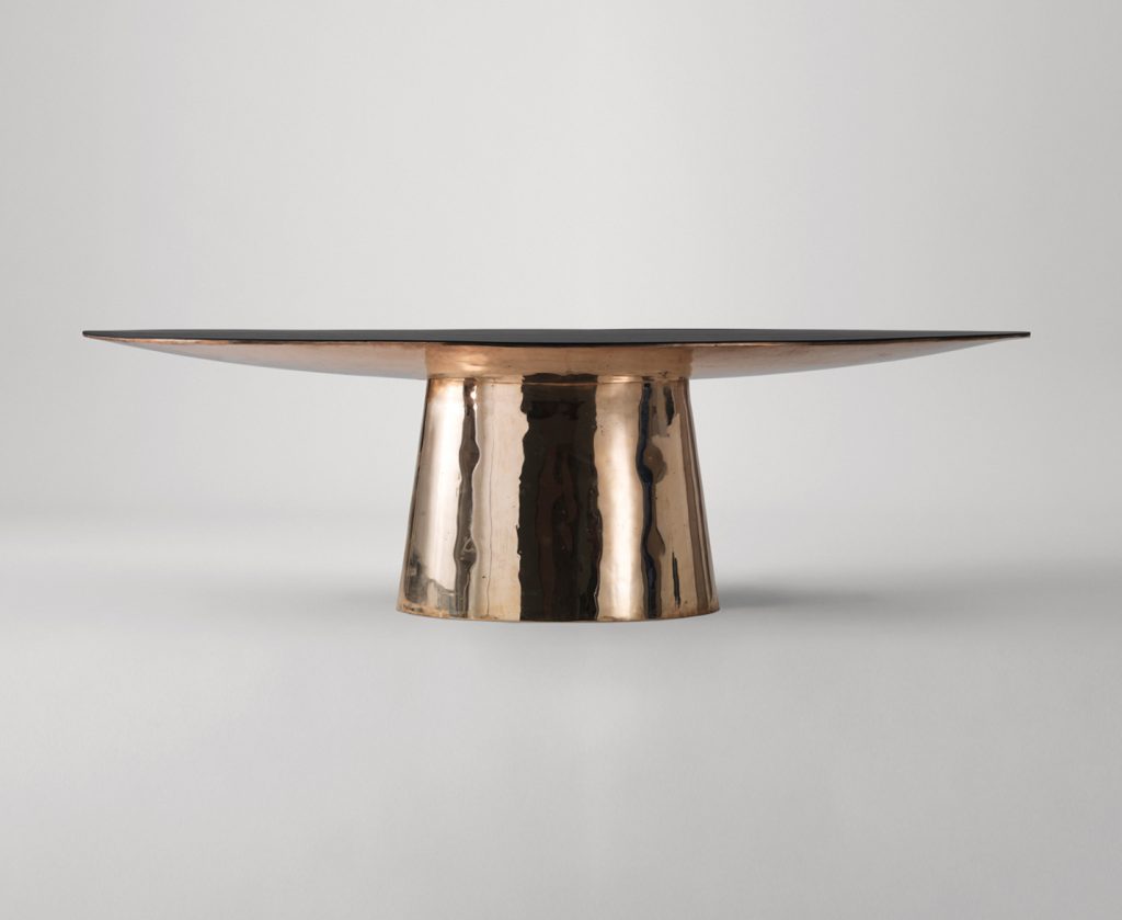 oval table made on a wooden base and lightly covered with leather and veneer in a golden colour tone on a white background