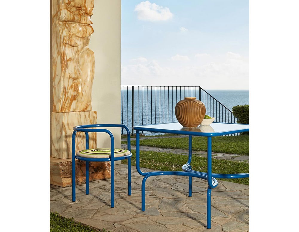 Locus Solus Chair with armrest. Struture in blue metal and multicolored cushion on a terrace.