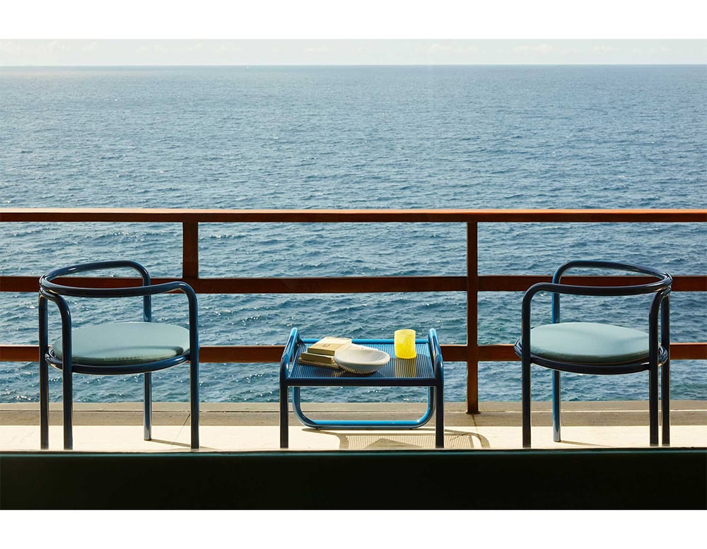 Two Locus Solus Chairs with armrest. Struture in blue metal and cushion on a terrace.