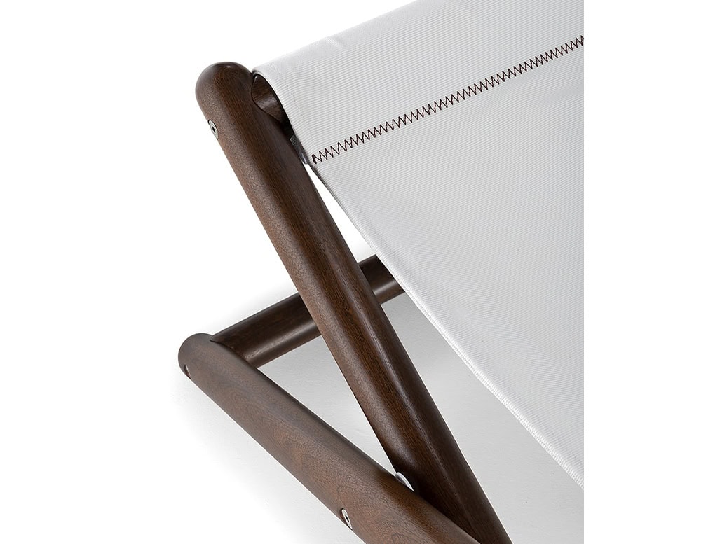 Closeup of Paraggi chair with crossed legs made of brown wood, upholstered in white fabric on a white background.