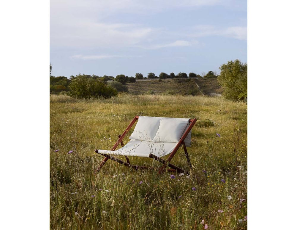 Paraggi chair with crossed legs made of brown wood, upholstered in white fabric on the countryside.