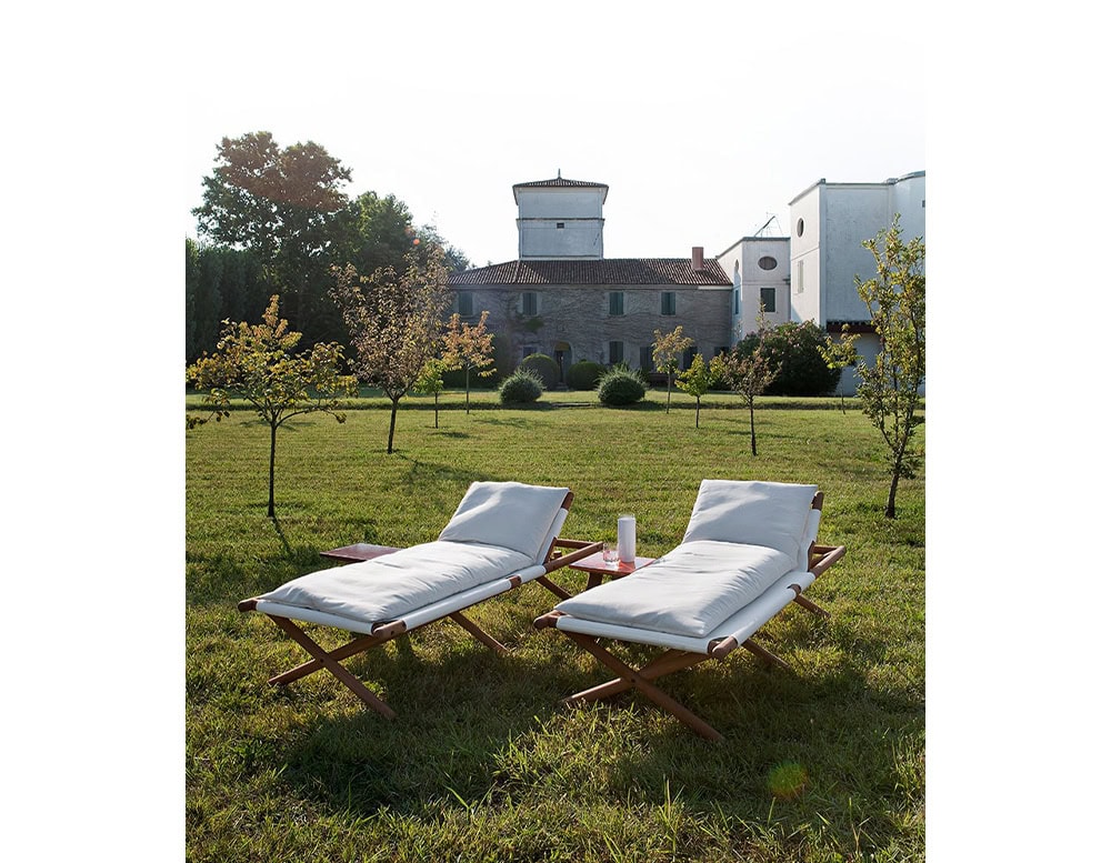 Paraggi Sun Lounger in brown wood upholstered in white fabric in a garden.