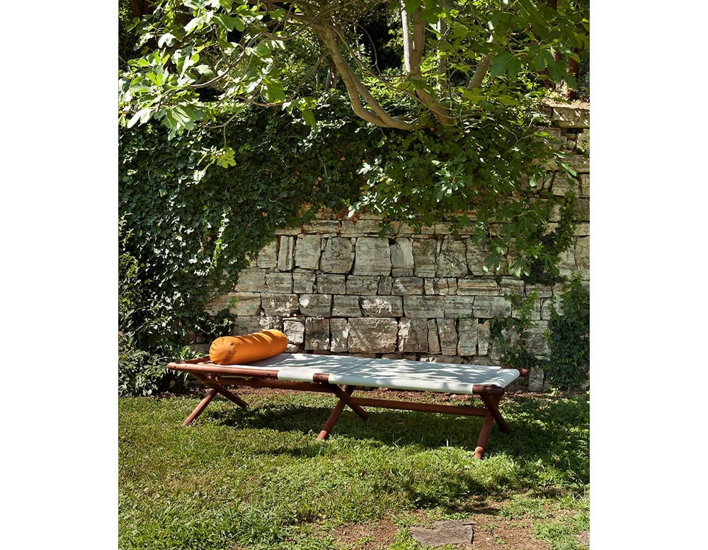 Paraggi Sun Lounger in brown wood upholstered in white fabric with orange cushion in a garden.