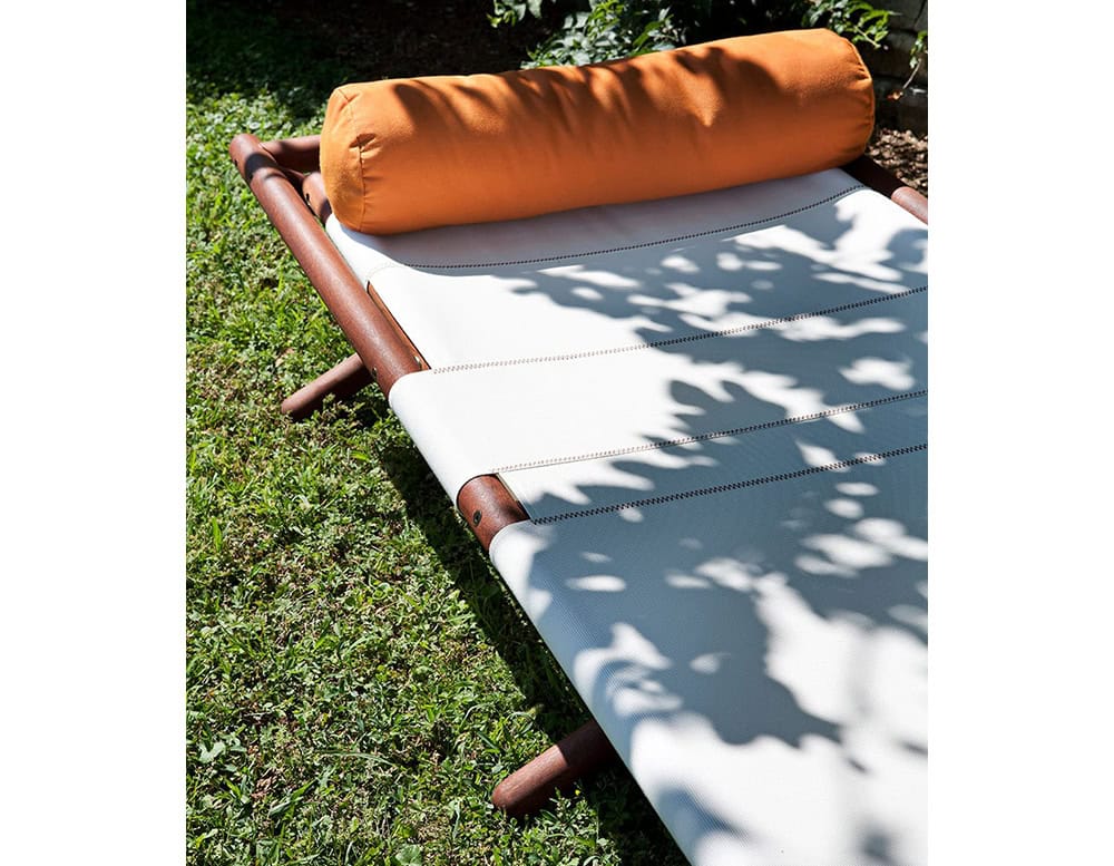 Paraggi Sun Lounger in brown wood upholstered in white fabric with orange cushion in a garden.