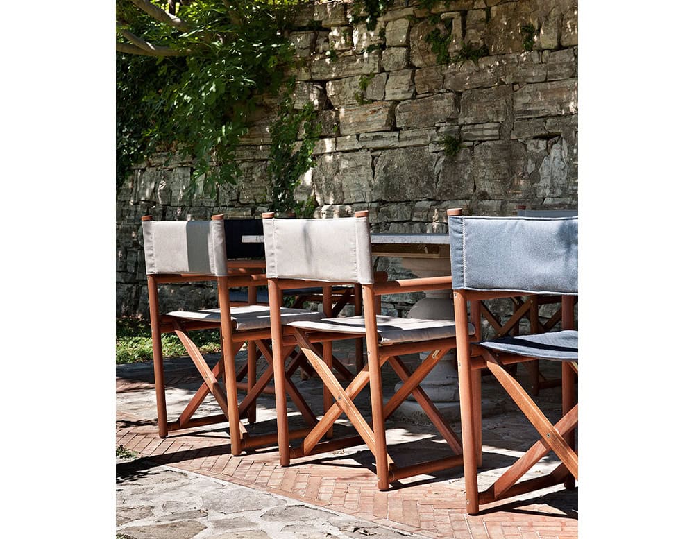 Three Paraggi Yacht Chairs. Structure in brown wood, seat and backrest upholstered in blue and gray fabric on a terrace.