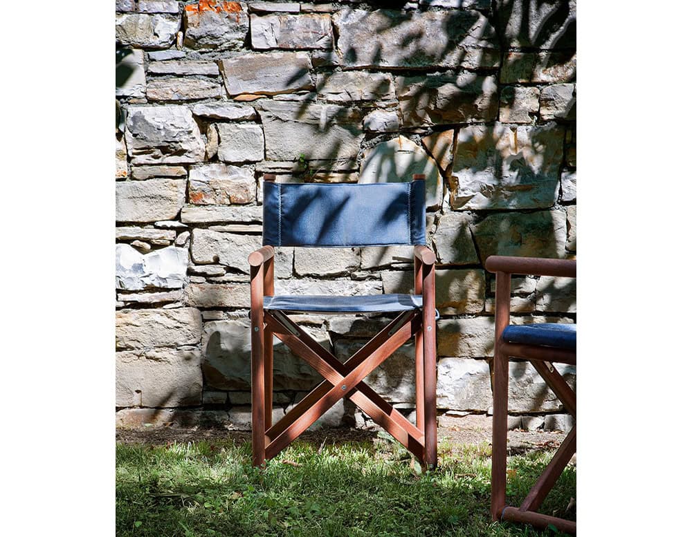 Paraggi Yacht Chair. Structure in brown wood, seat and backrest upholstered in blue fabric in a garden.