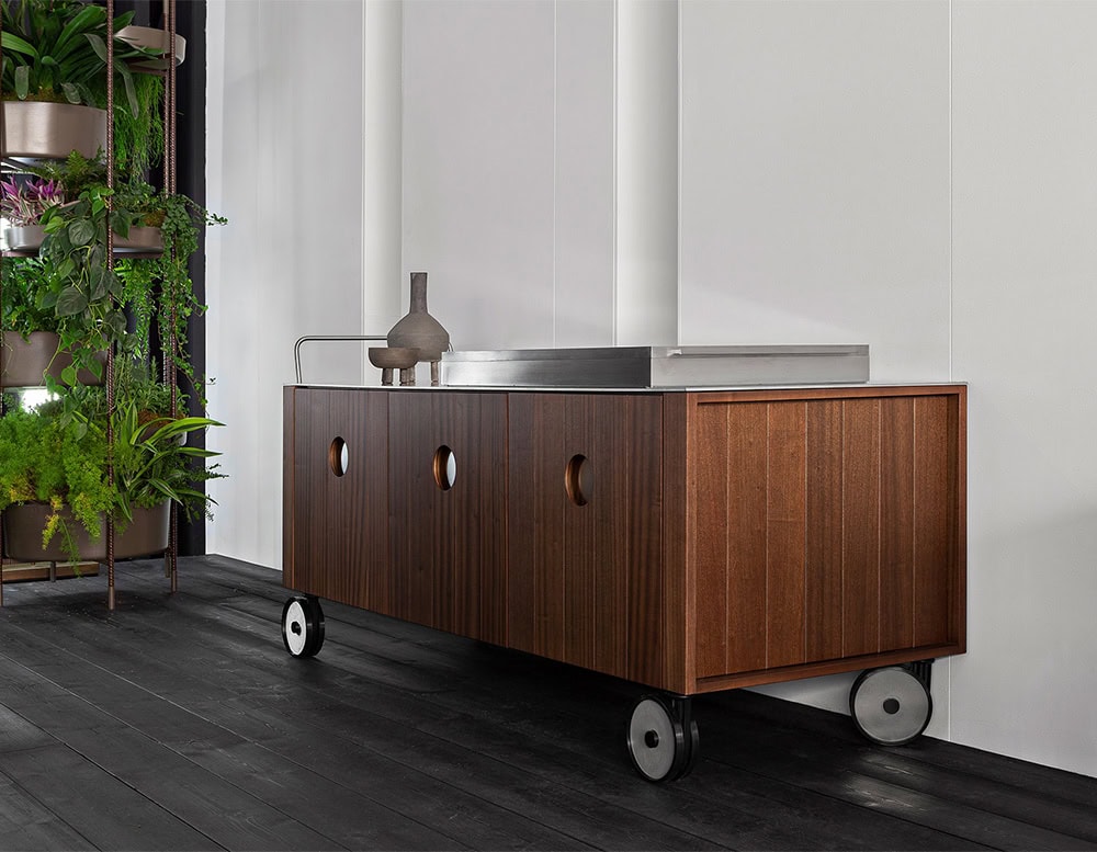 Roller Kitchen cabin covered in brown wooden with four wheels against a wall.