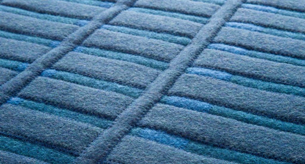 Accordi rug. The surface of the rug consists of blue anternated stripes and horizontal and vertical felt stripes.