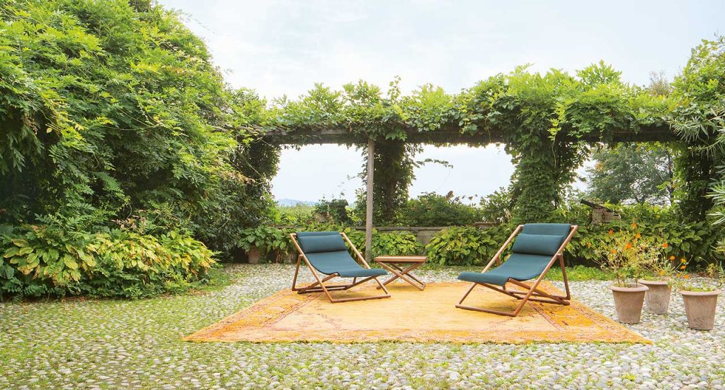 Two Portofino Outdoor Deck Chairs, structure in natural heartwood, upholstery in blue fabrics in a garden.