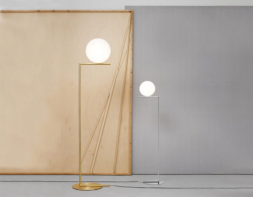 One Flos IC floor lamp that is tall and facing another Flos IC floor lamp that is shorter against a gray and tan colored wall.