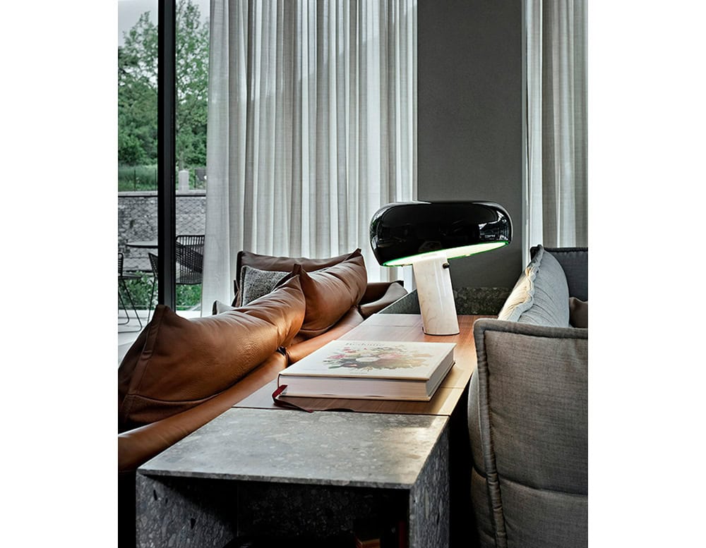 Flos Snoopy table lamp atop a wood tabletop between the backside of two sofas.