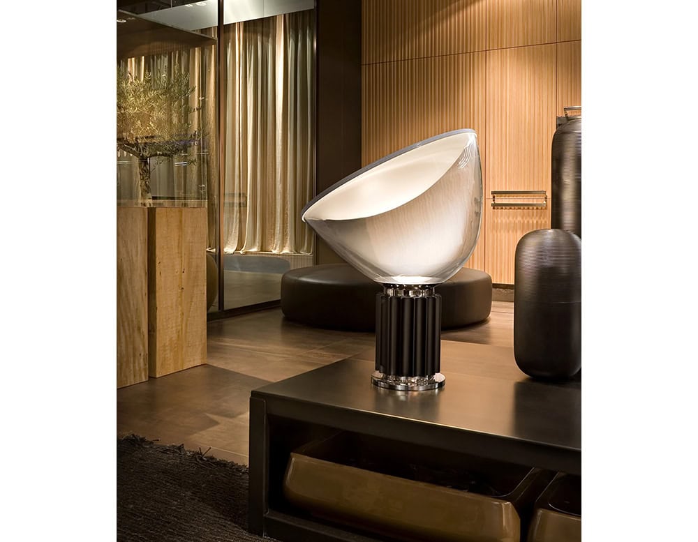 Flos Taccia on a black coffee table surrounded by a black ottoman in the back and a wooden credenza to the left.