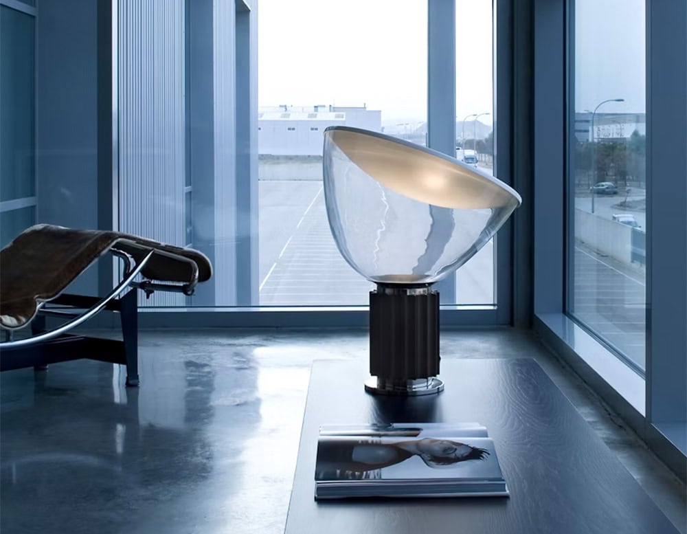 Flos Taccia table lamp on top of a credenza in room of bright windows with a lounge chair on the side.