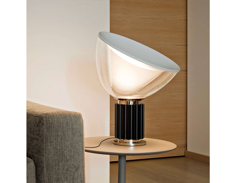 Flos Taccia lamp on a circular table next to the edge of a gray sofa arm rest.